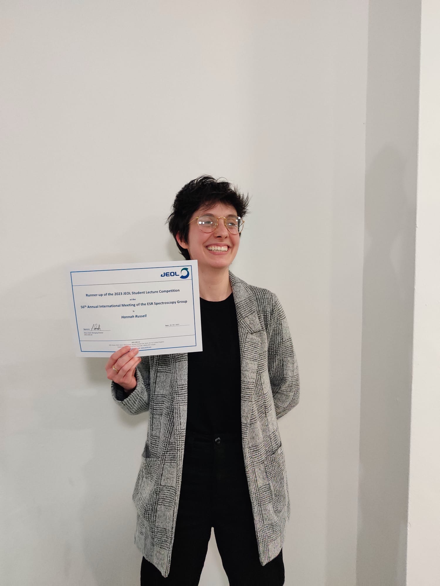 Hannah Russell smiling and holding a certificate showing that she was runner up in the Jeol student prize talks.
